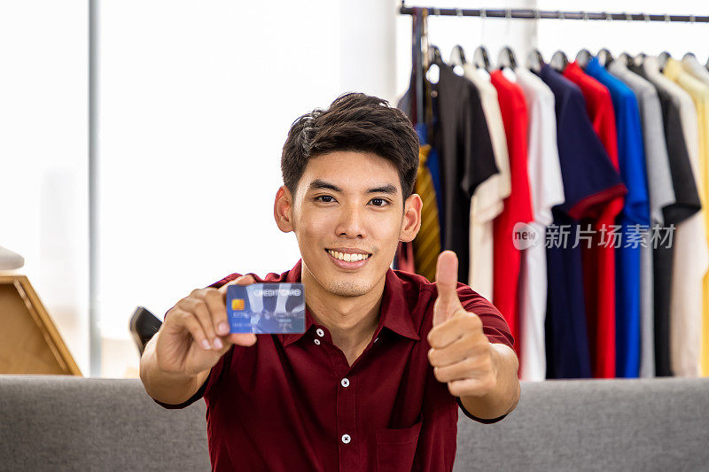 Young Asian male online merchant blogger live video to sell, holding credit card, with thumb up, looking at camera. Social media, Influencer, online shopping, and payment concept.